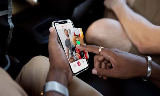 A person in the driver's seat holds a smartphone while a passenger sits beside them in the vehicle creating good Hinge answers to the I'm looking for prompt