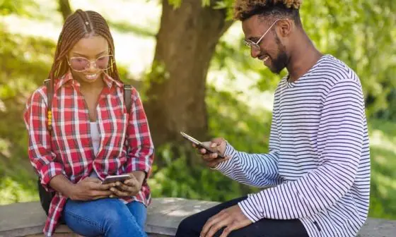 A pair of young people on a bench, focused on their phones, illustrating modern social interaction in a public space.