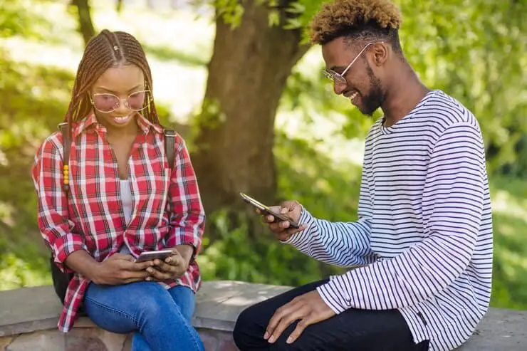 A pair of young people on a bench, focused on their phones, illustrating modern social interaction in a public space.