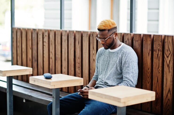 A man seated on a bench, focused on his phone where he uses the "I'm convinced that prompt", surrounded by a serene outdoor environment.