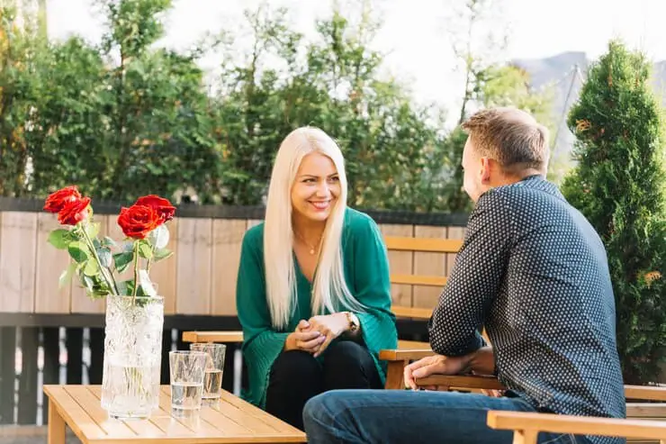 A man and woman engaged in discussion while sitting at a patio table in a relaxed outdoor setting